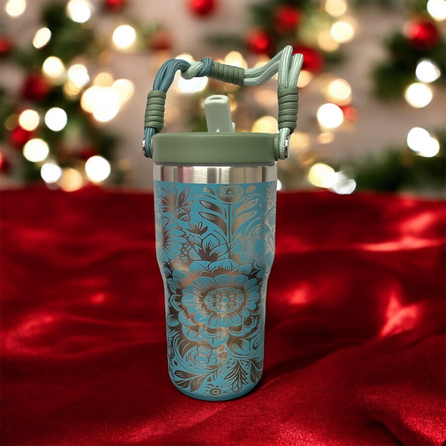 Blue floral-patterned tumbler with a green handle on a red surface with blurred Christmas lights in the background